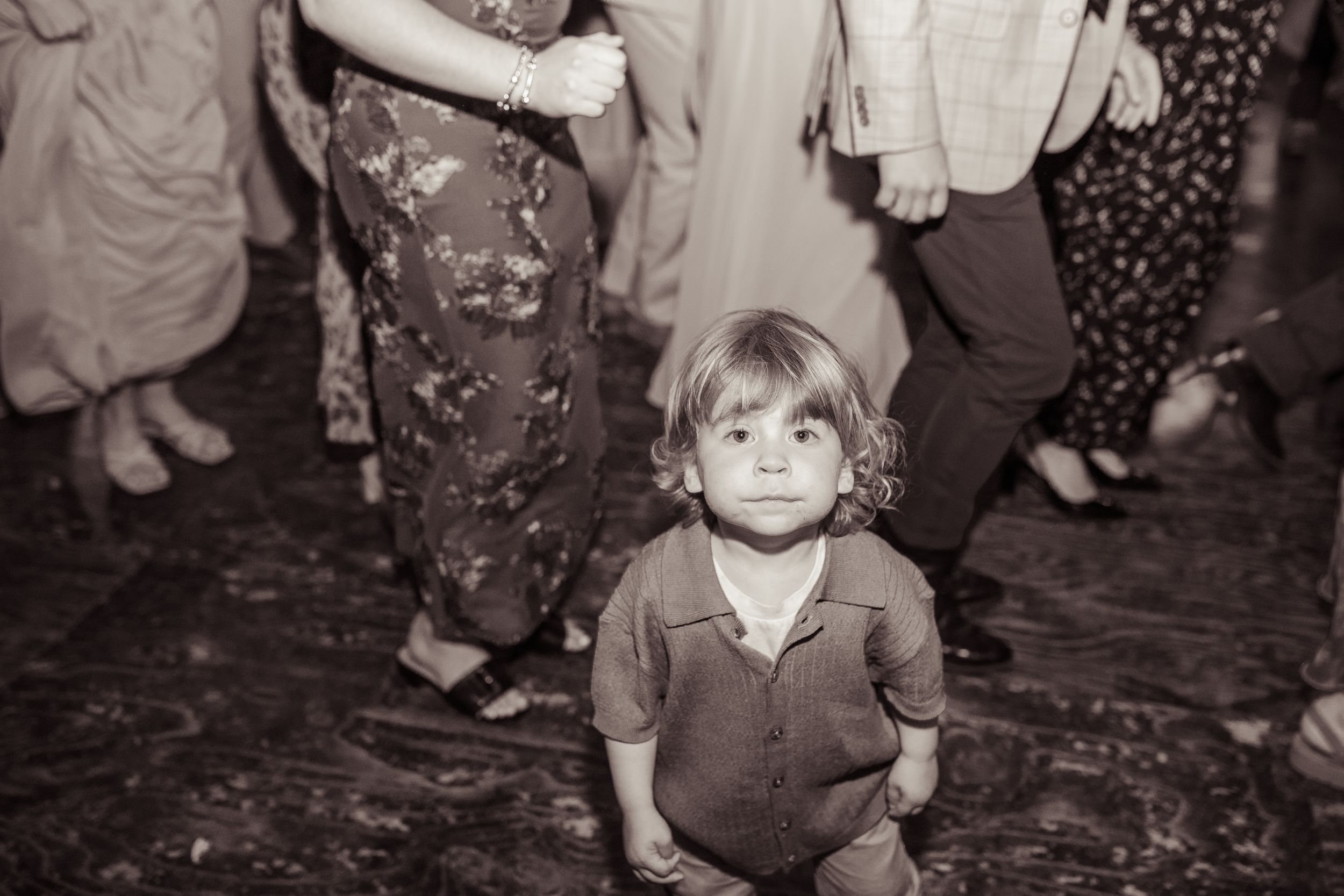 Adorable young child stands on dance floor surrounded by wedding guests during reception celebration.
