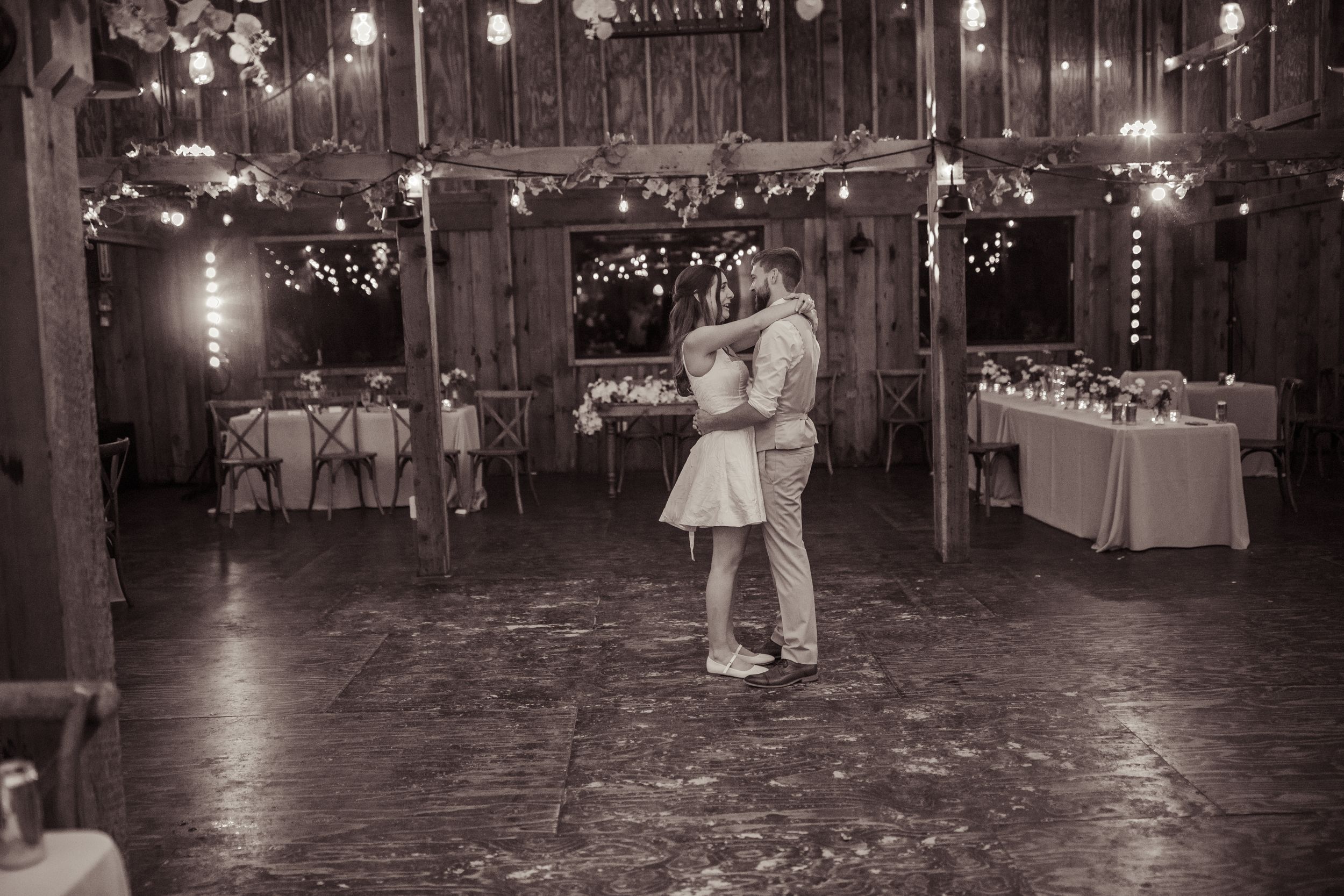 Black and white photo of bride and groom sharing their first dance alone in a rustic barn wedding venue.