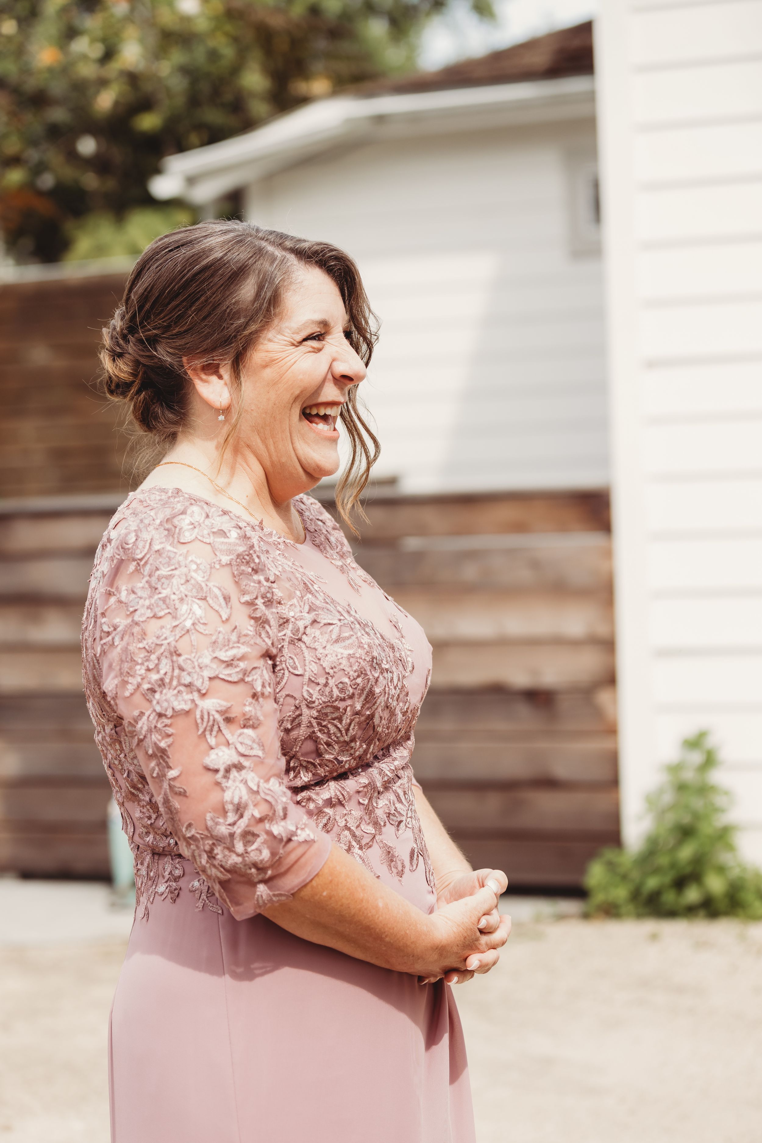 Woman in pink lace dress laughing outdoors at a wedding celebration.