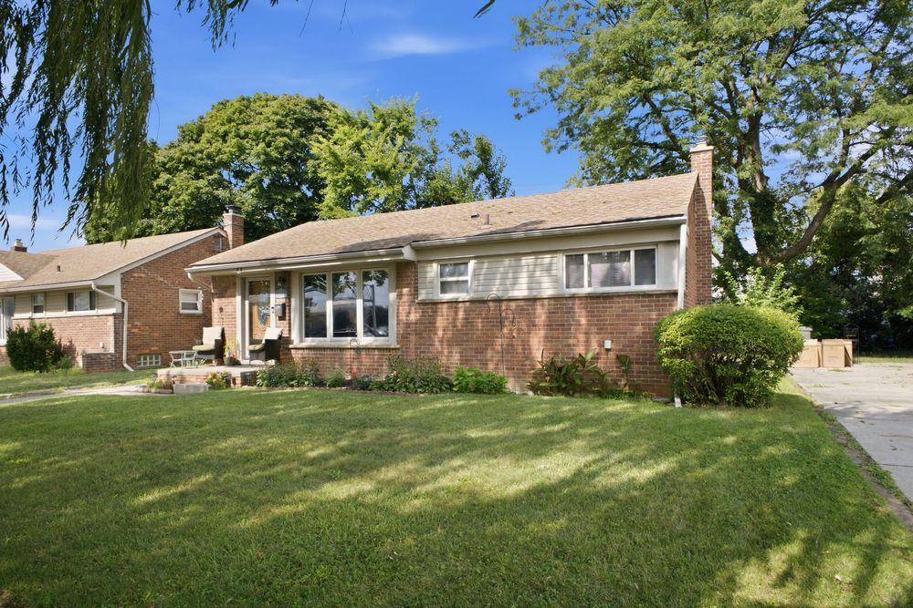 Brick ranch-style home with lush green lawn, mature trees, and well-maintained landscaping on a sunny day.