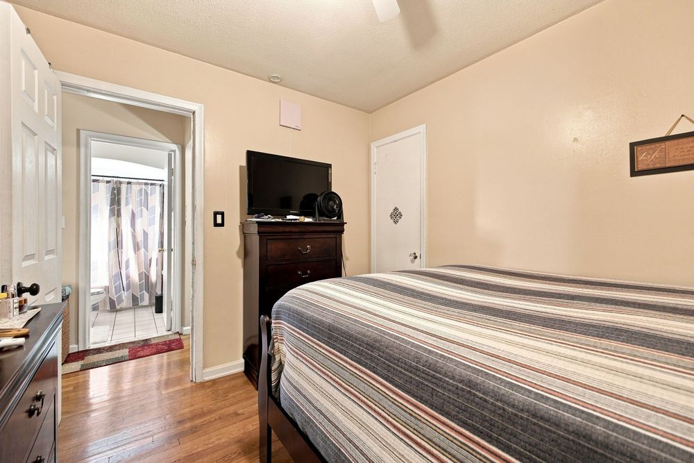 Cozy bedroom with hardwood floors, striped bedspread, dark wood dresser with TV, and door leading to sunlit patio.