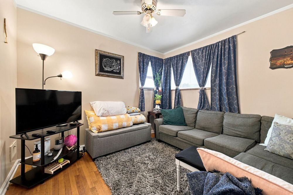 Cozy living room with gray sectional sofa, flat-screen TV, hardwood floors, ceiling fan, and blue curtained windows.