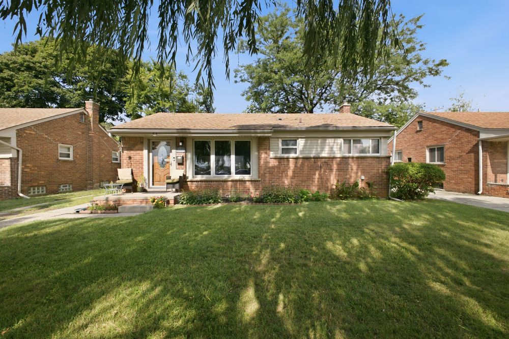 Brick ranch-style home with lush green lawn, large shade trees, and well-maintained landscaping on a sunny day.