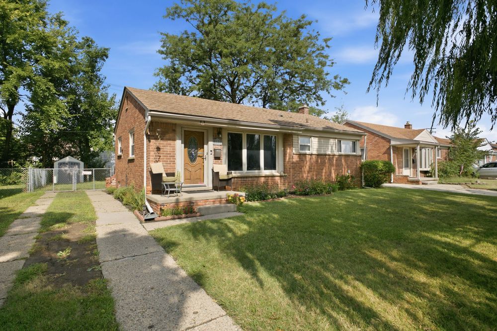 Brick ranch-style home with lush green lawn, large shade trees, and a welcoming front porch on a sunny day.