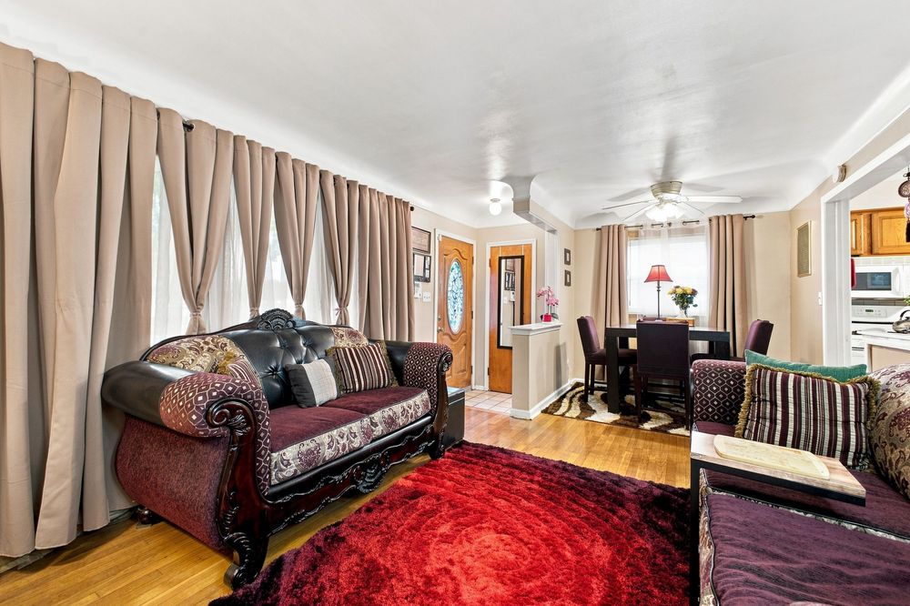Cozy living room with dark leather sofa, red rug, hardwood floors, and dining area visible in background.