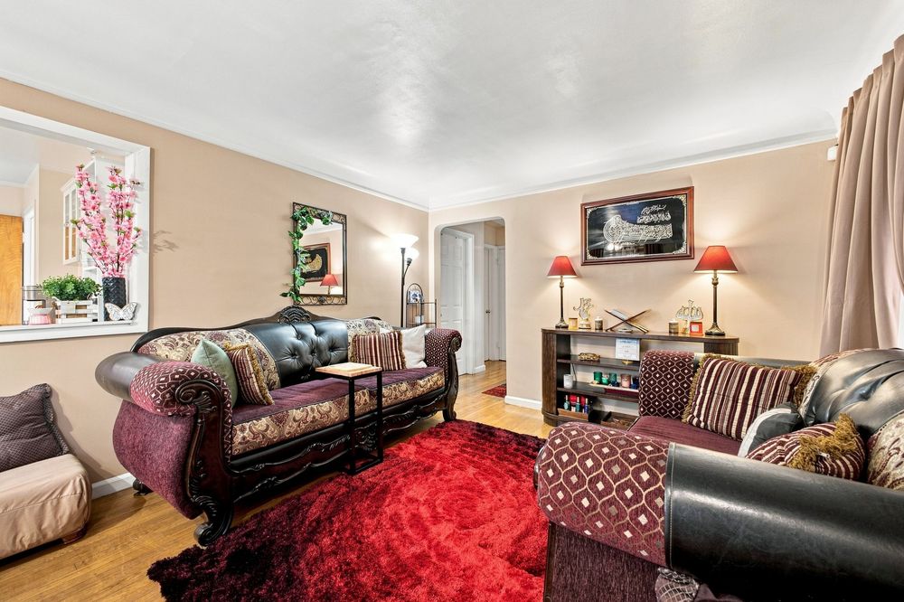 Cozy living room with red patterned rug, leather sofas, warm lighting, and elegant decor on hardwood floors.