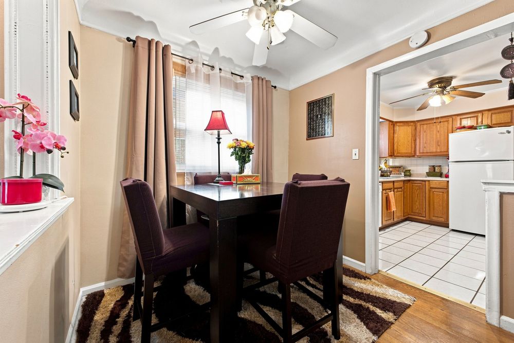 Cozy dining room with dark wood table, burgundy chairs, ceiling fan, and view into kitchen with white appliances.