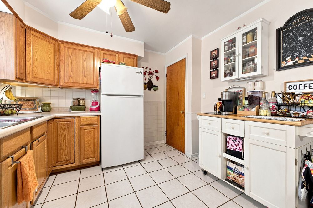 Kitchen with oak cabinets, white refrigerator, tile floors, and a coffee station with white upper cabinets.