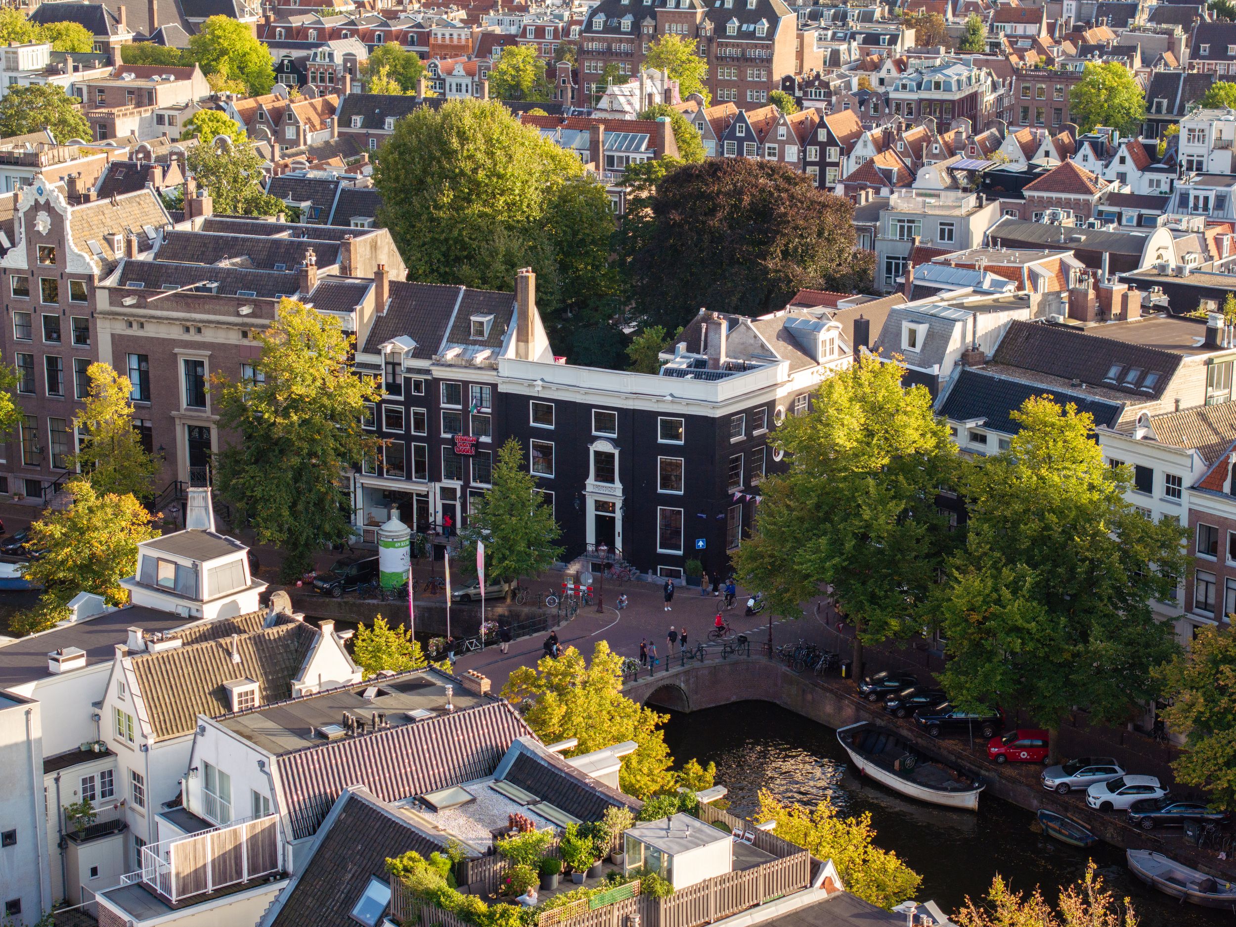 Aerial view of Amsterdam canal district with historic brick buildings and lush green trees in golden hour light.