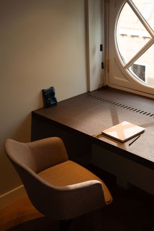 Minimalist dark wood desk with notepad and pencil beside a round arched window with a beige swivel chair.