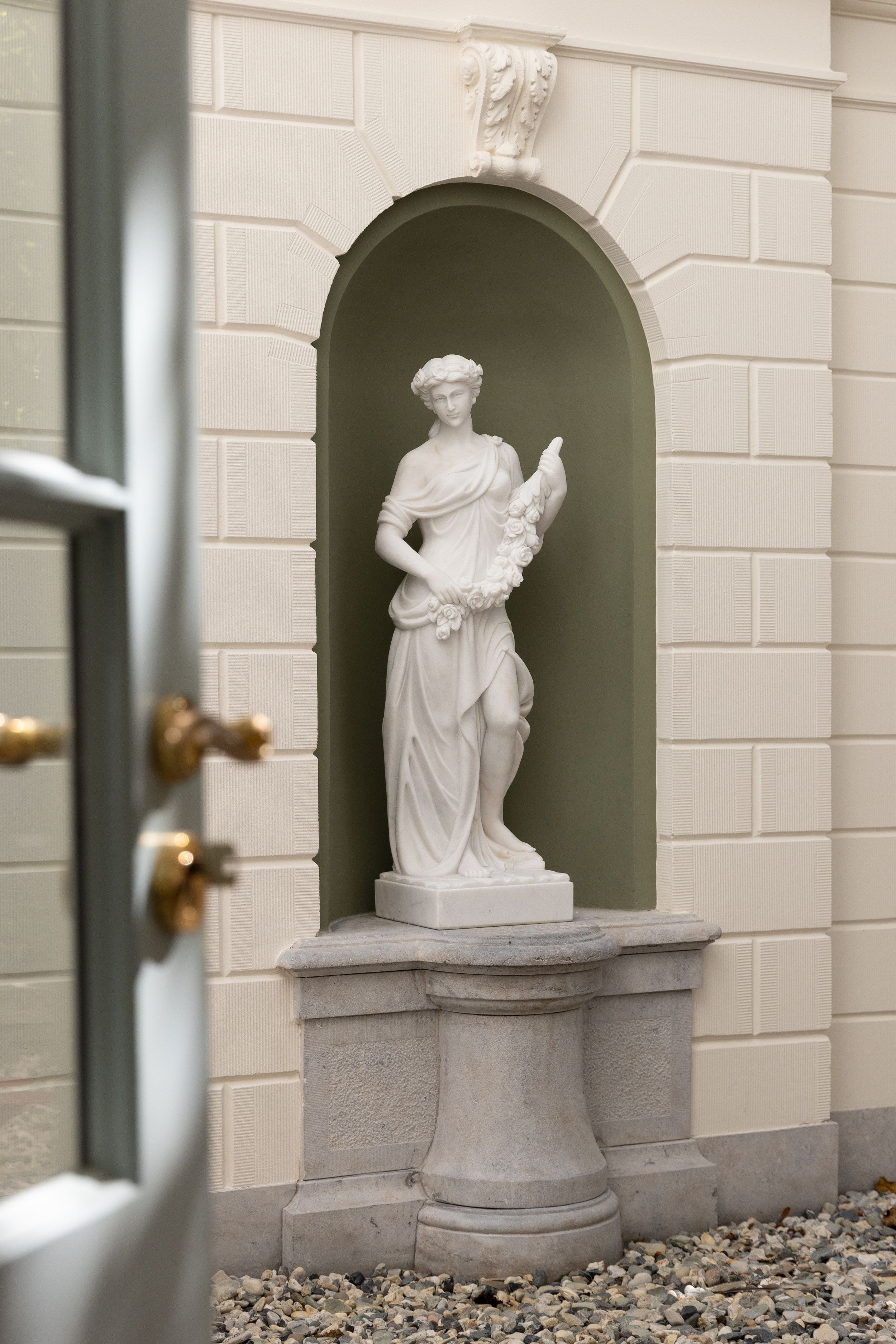 White classical female statue holding a cornucopia, displayed in an arched niche on a marble pedestal.