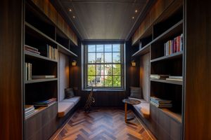 Elegant library reading nook with dark wood built-in shelves, herringbone parquet floor, and large window overlooking greenery.