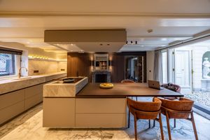 Modern luxury kitchen with marble island, brown dining chairs, and seamless indoor-outdoor living space.