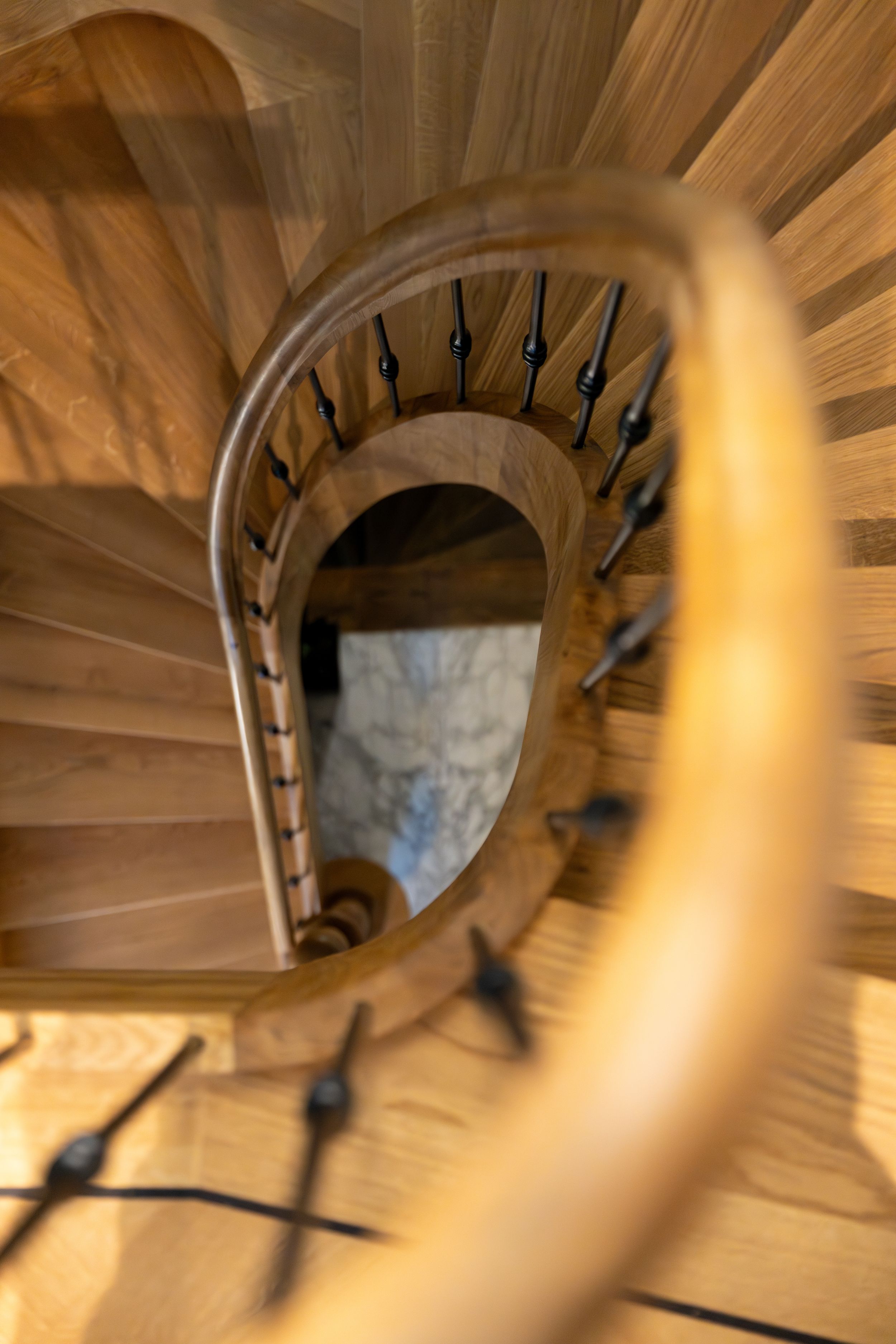 Aerial view of an elegant wooden spiral staircase with black iron balusters and a curved handrail.