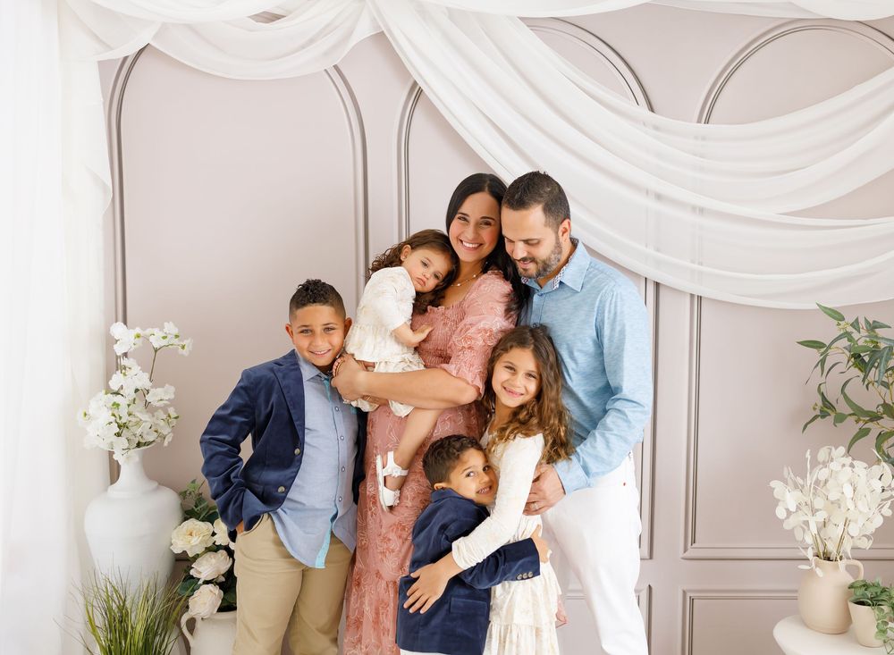 An elegant indoor photo session setup with white drapes and floral decorations against a gray wall.
