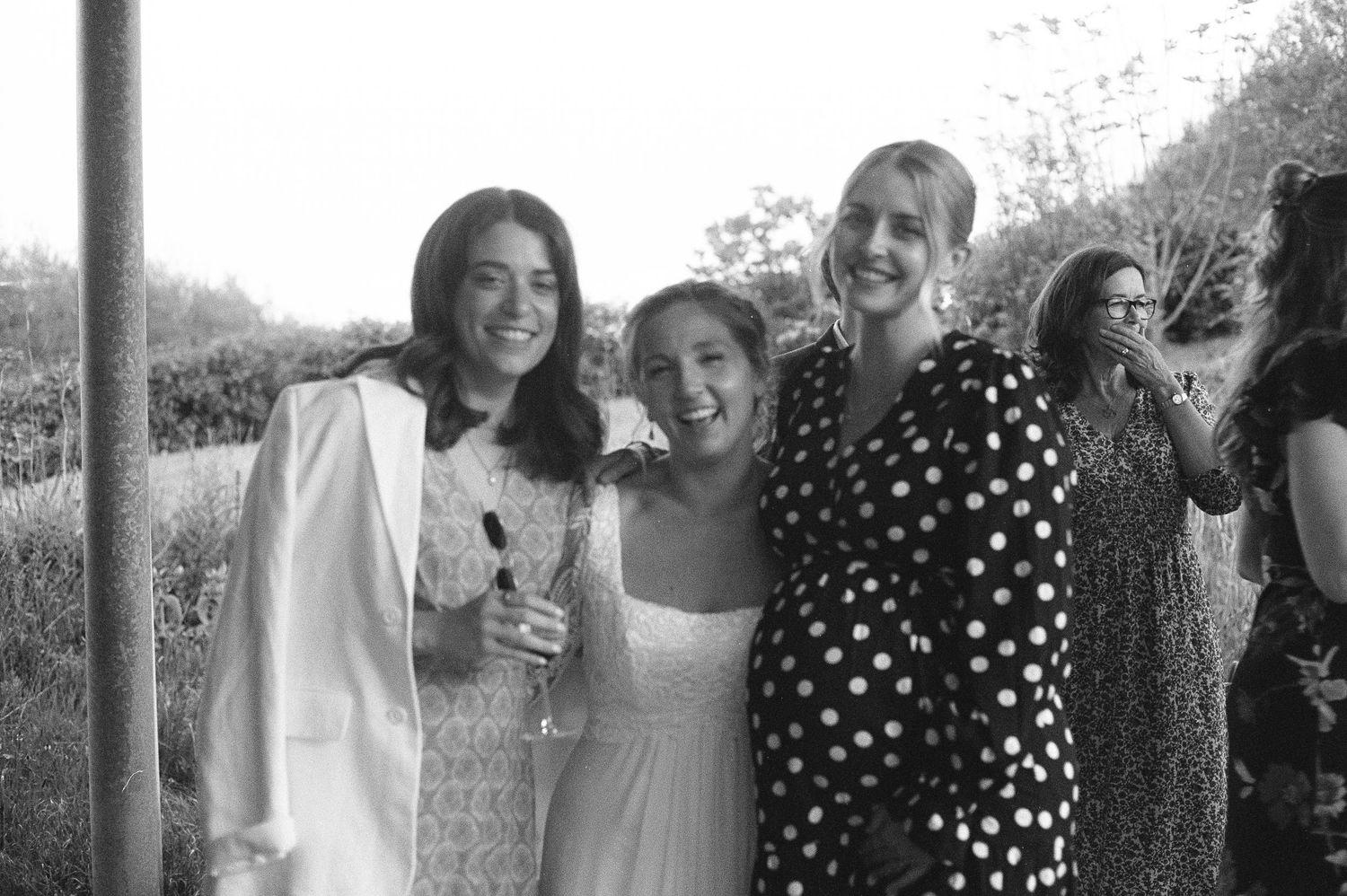 Three women smiling and posing together outdoors at a social gathering in black and white photo.