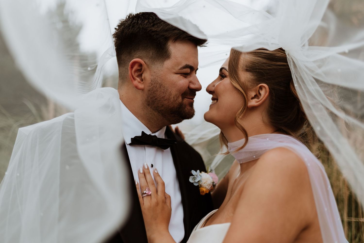 Bride in white gown with veil and groom in black suit walking toward a red brick castle venue.