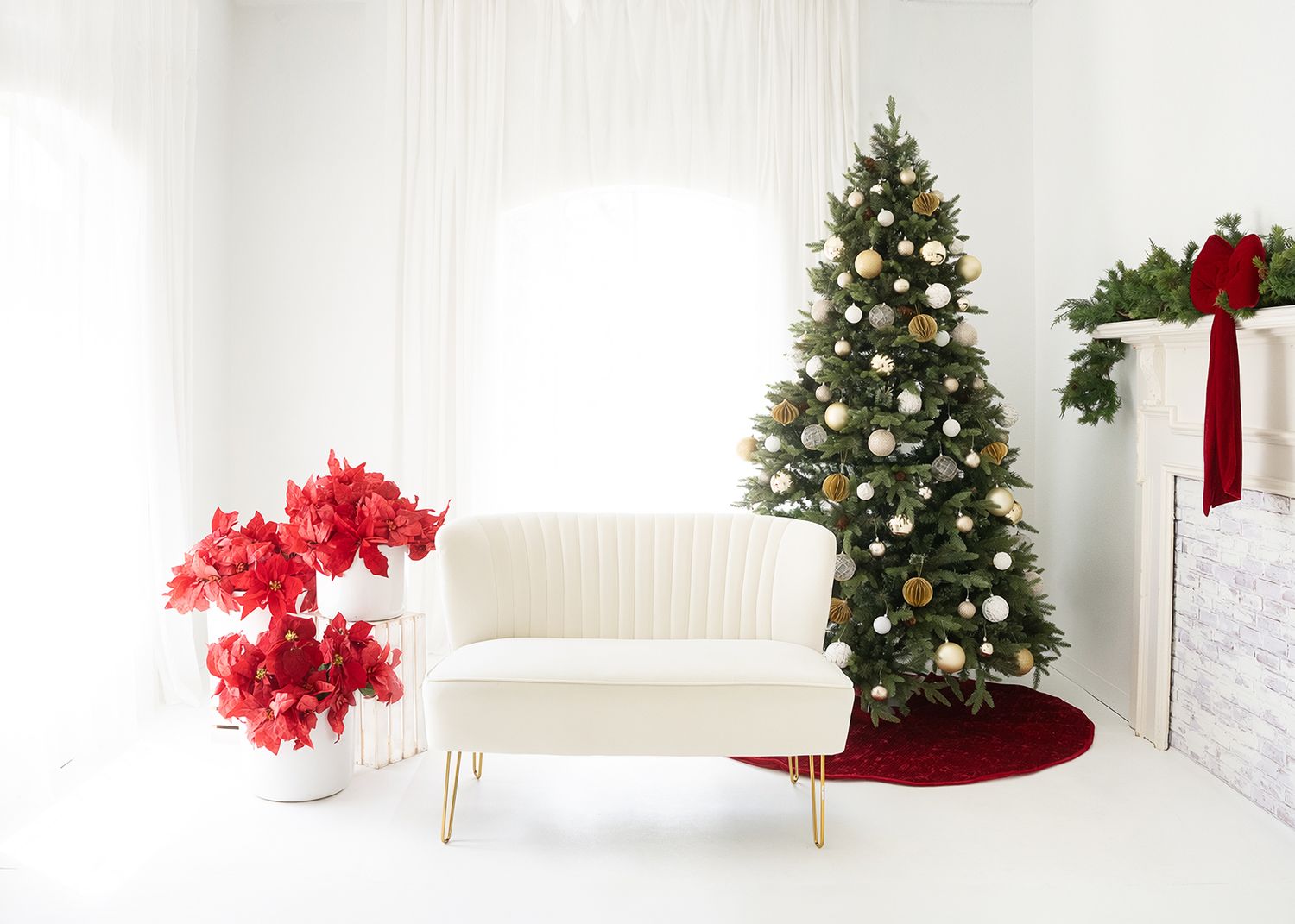 White living room with cream loveseat, decorated Christmas tree, red floral arrangement, and festive holiday decor.