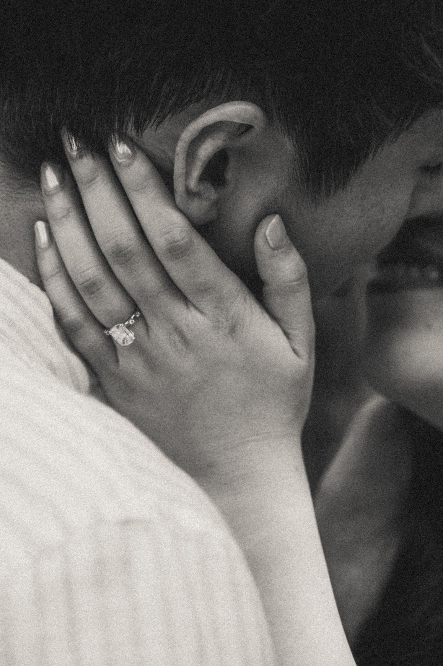 Black and white photo of a couple embracing, showcasing a diamond engagement ring on the woman's hand.