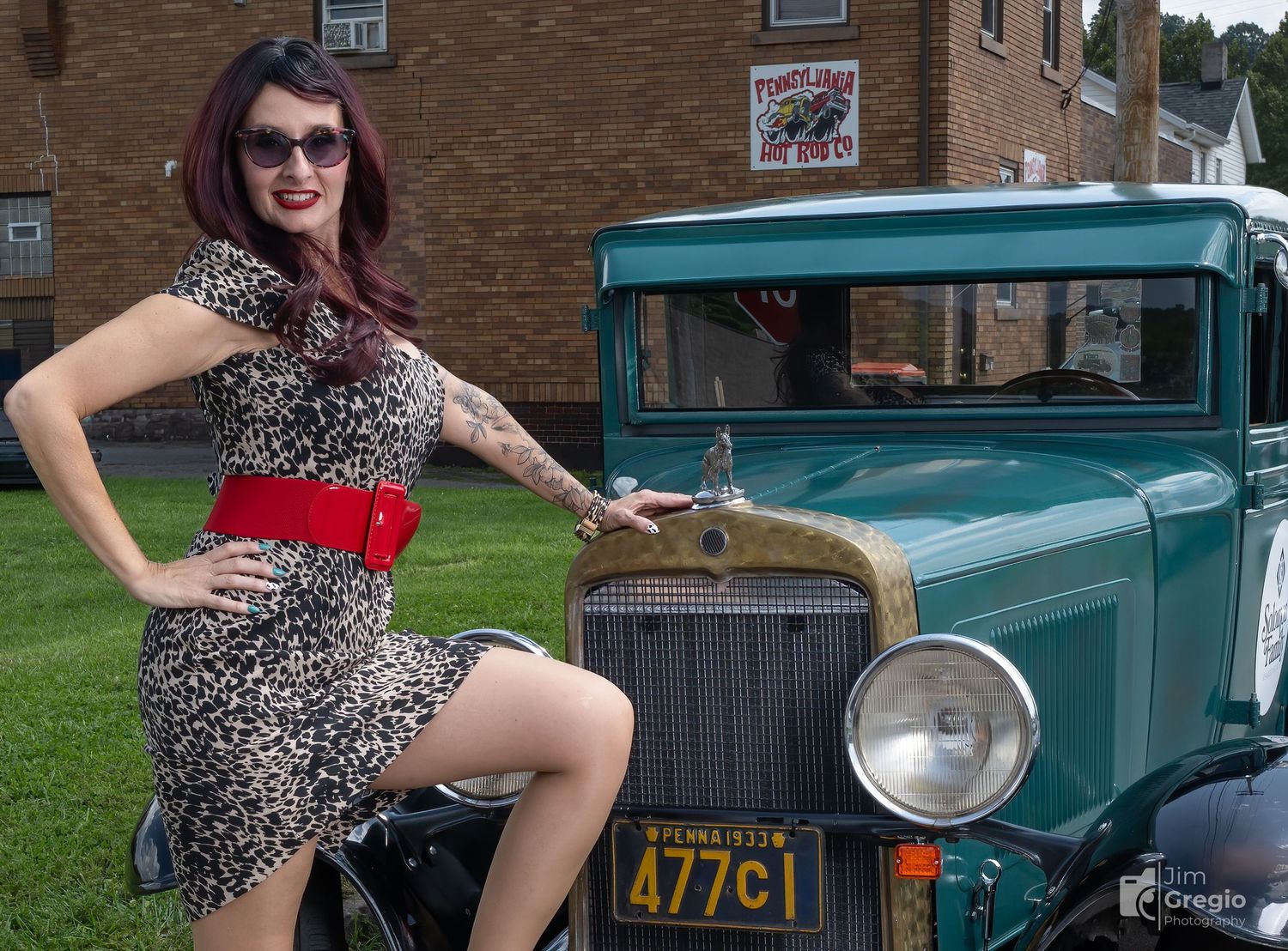 Woman in leopard print dress poses beside a vintage teal classic car with Oregon license plate outdoors.