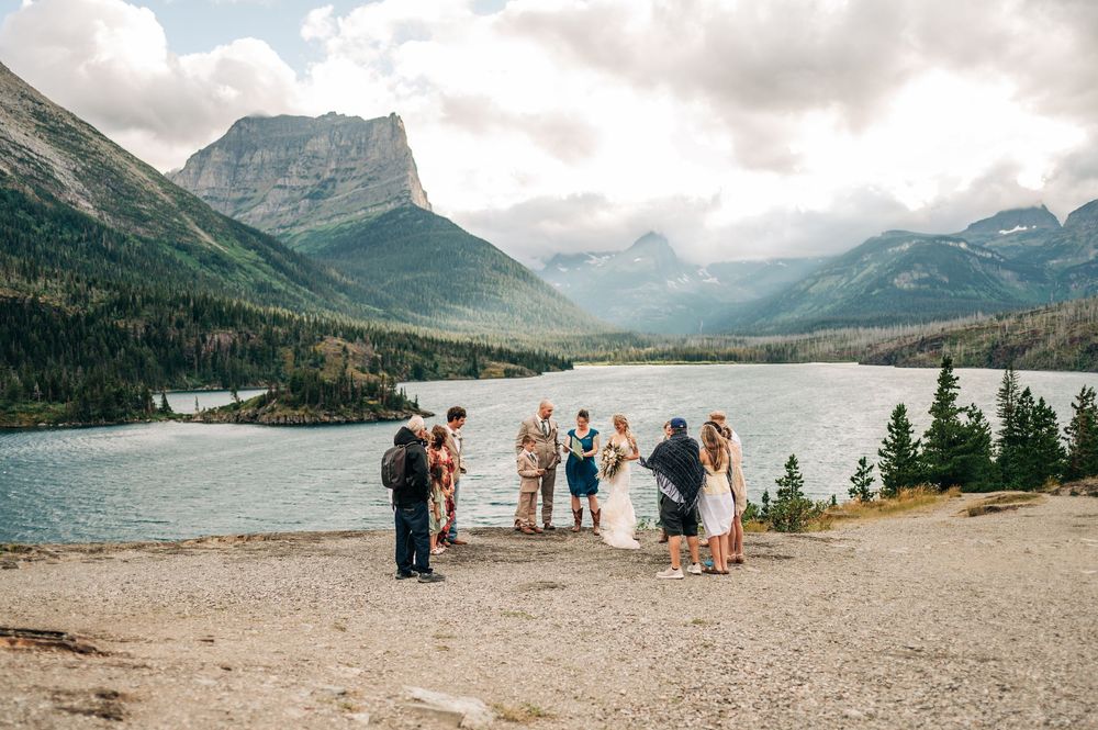 Small wedding ceremony outdoors by a mountain lake with stunning peaks and cloudy skies in Glacier National Park.