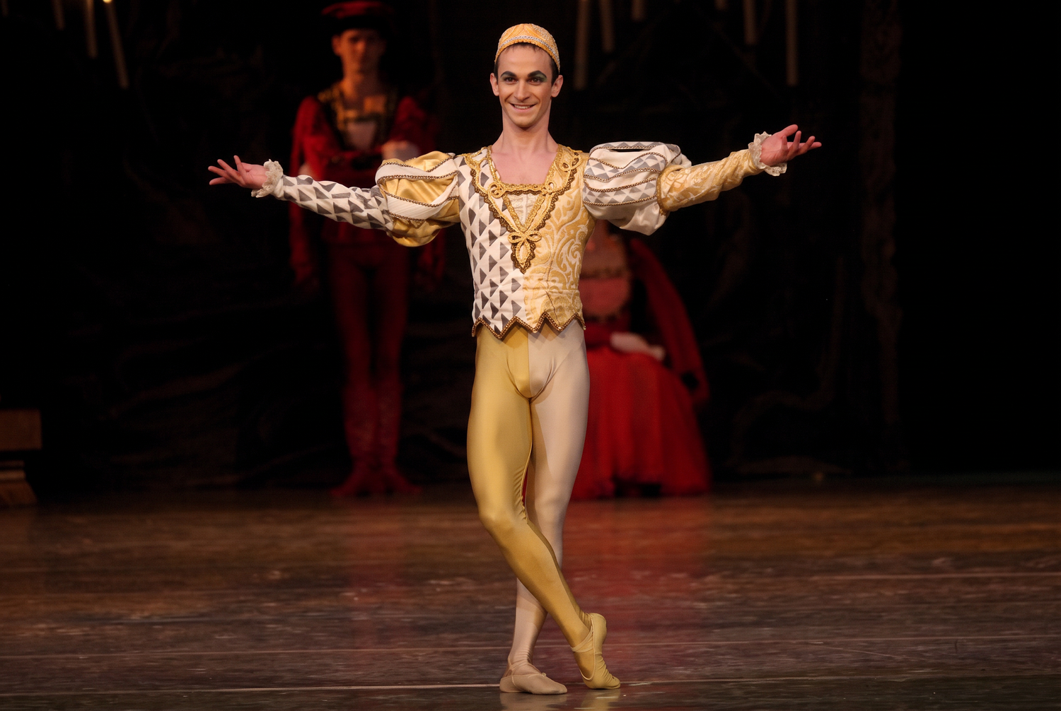 Male ballet dancer in golden costume performs on stage with arms outstretched in a graceful pose. Juraj Zilincar