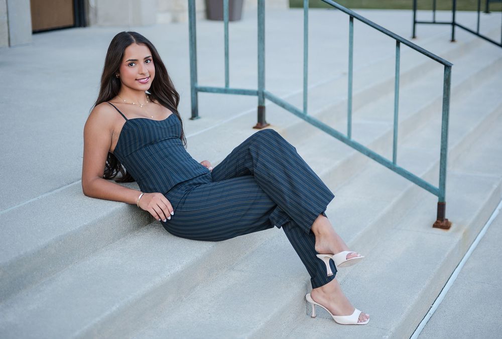 Young woman in striped jumpsuit and white heels posing on outdoor steps in an urban setting.