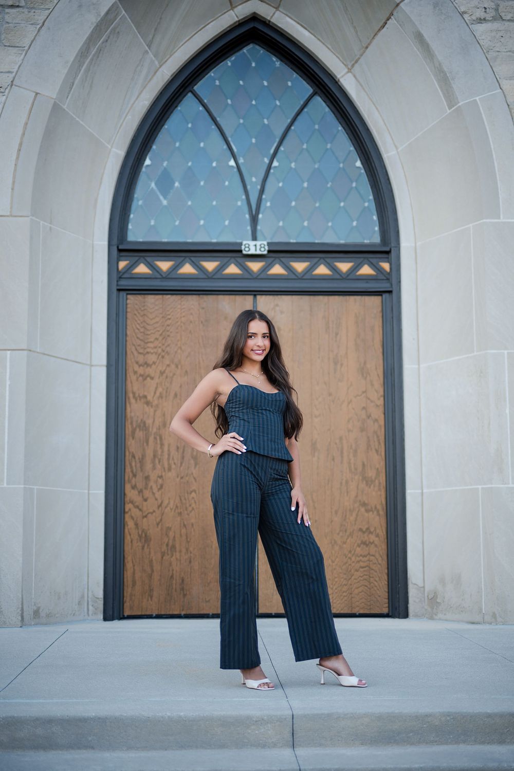 Woman in striped jumpsuit posing confidently before an arched Gothic church door with stained glass window.