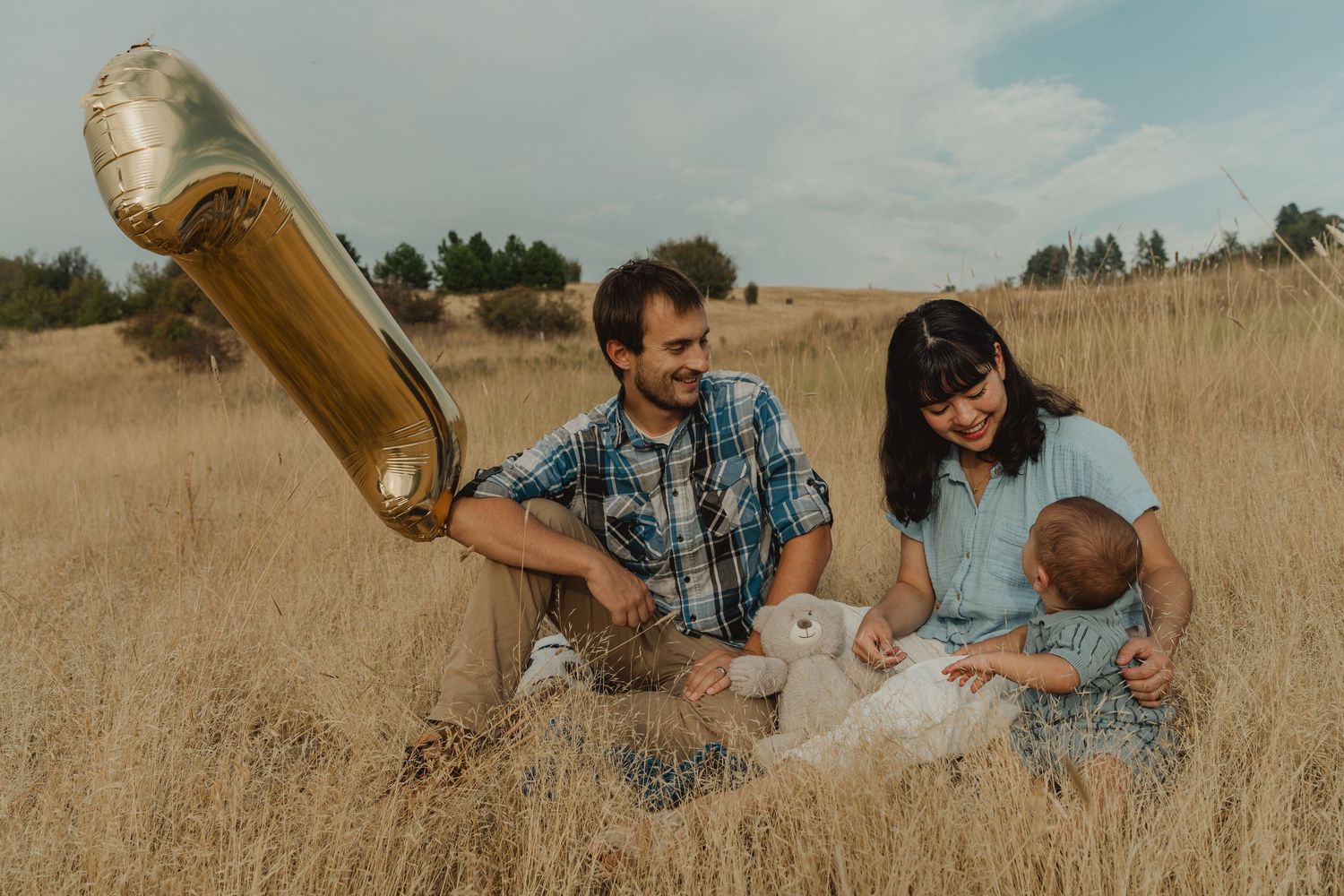 Parents and baby spending time together on a blanket in the field during a first birthday family session.