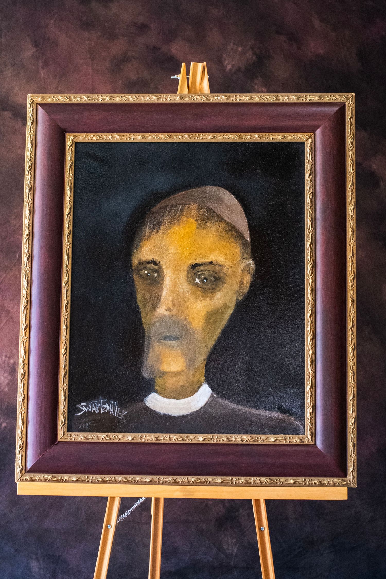 Dark expressionist portrait painting in ornate gold and burgundy frame displayed on wooden easel.