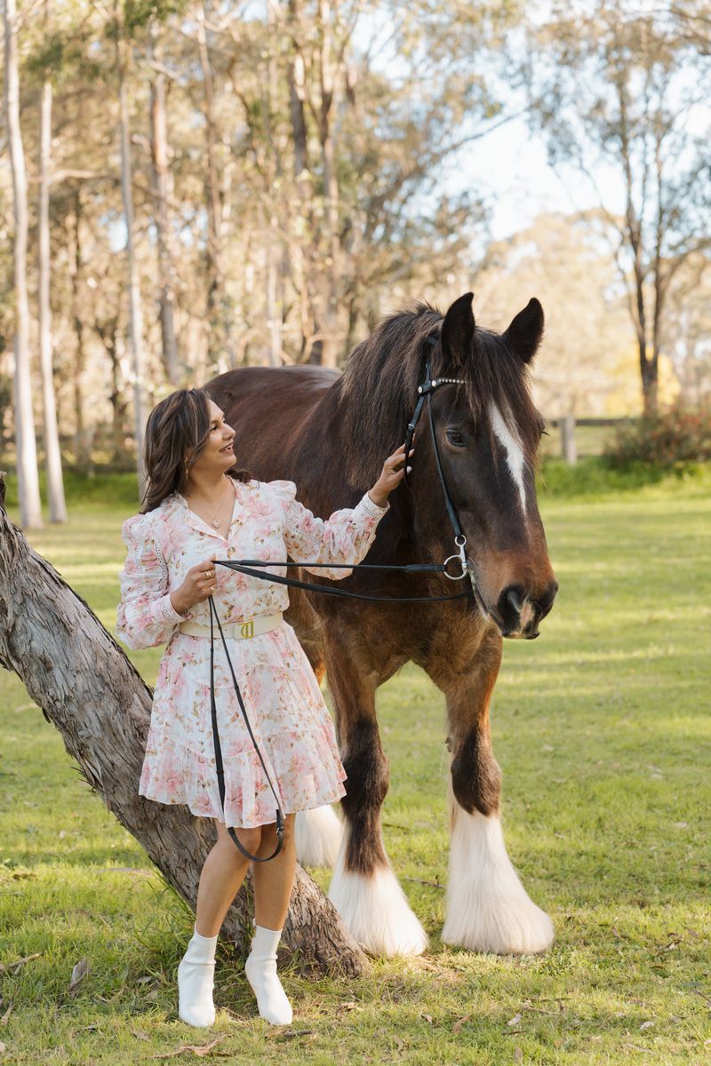 Woman in floral dress petting a brown Shire horse beside a tree in Sydney Hawkesbury during a photoshoot