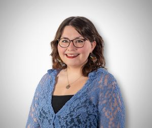 Smiling woman with glasses wearing a blue lace cardigan and necklace poses for a professional headshot. Quad Cities Photography