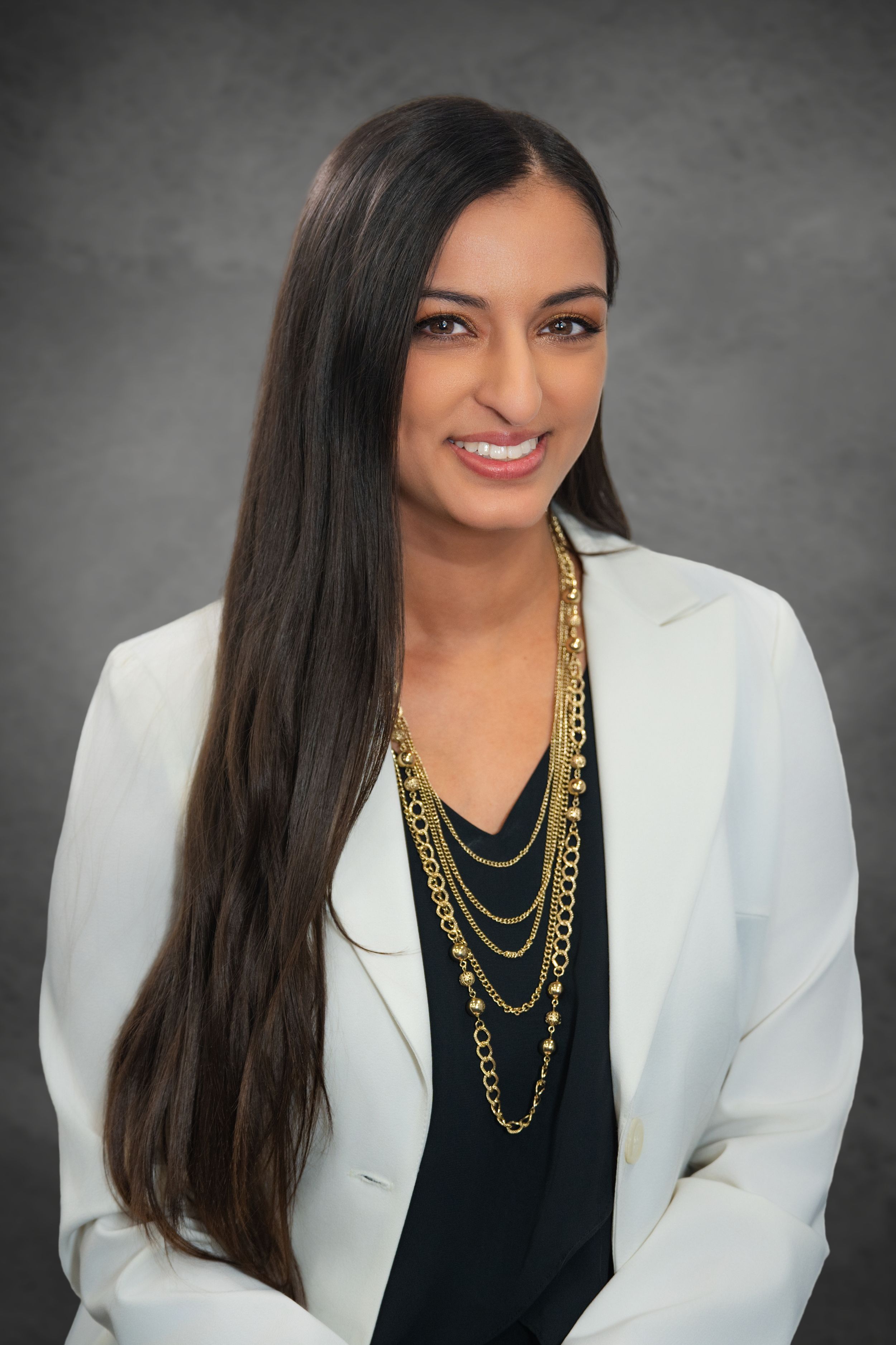 Professional woman in white blazer and gold layered necklaces smiling against gray studio background.  Quad Cities Photography