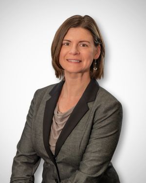 Professional woman in gray blazer with black lapels, brown bob haircut, smiling confidently against white background.  Quad Cities Photograp