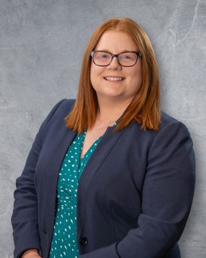 Professional headshot of a smiling woman with red hair and glasses wearing a teal blouse and navy blazer.  Quad Cities Photography