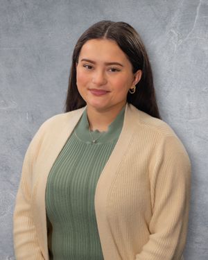 Young woman with long dark hair wearing a green top and cream cardigan, smiling professionally against a gray background.  Quad Cities Photo