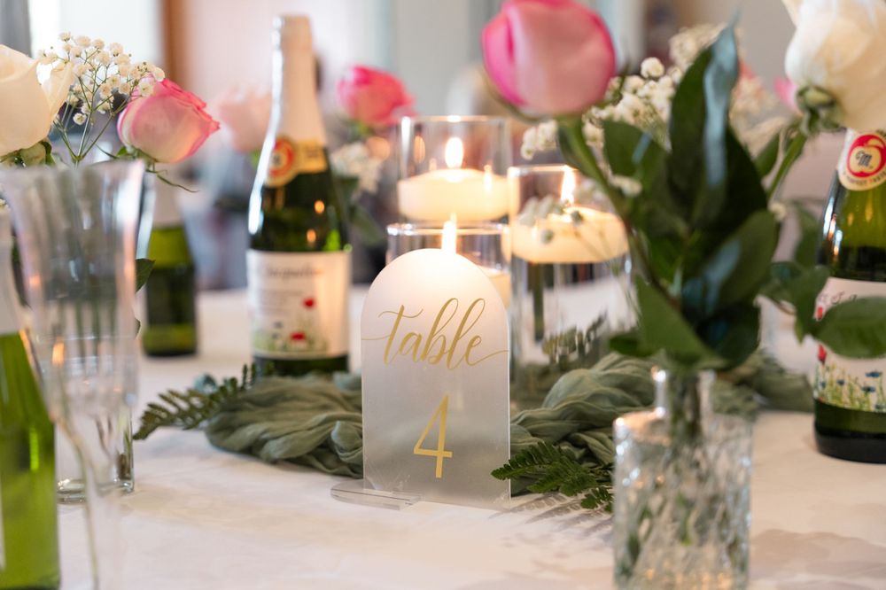 Elegant table setting with frosted glass candle holders, floral arrangements and eucalyptus leaves on a white tablecloth.