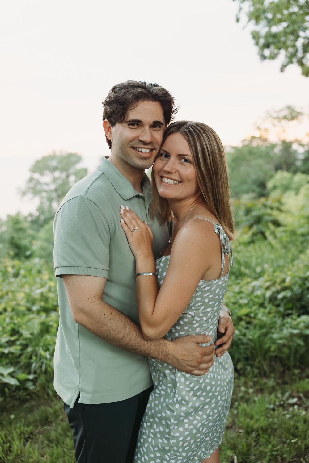 Smiling couple embracing outdoors in green nature setting, wearing coordinating mint outfits in a romantic portrait photo.