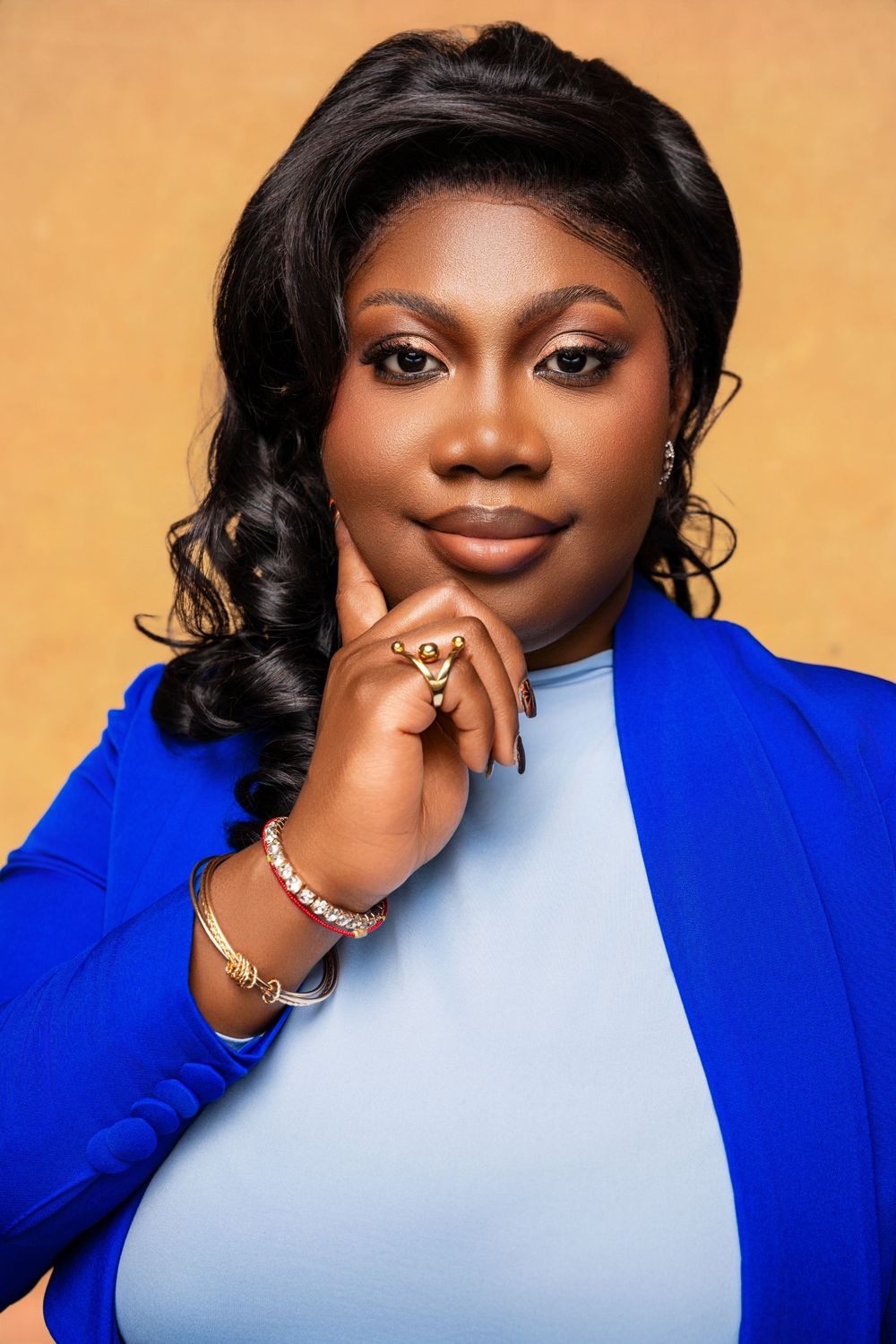 Professional woman in blue blazer posing confidently against golden background, wearing gold jewelry.