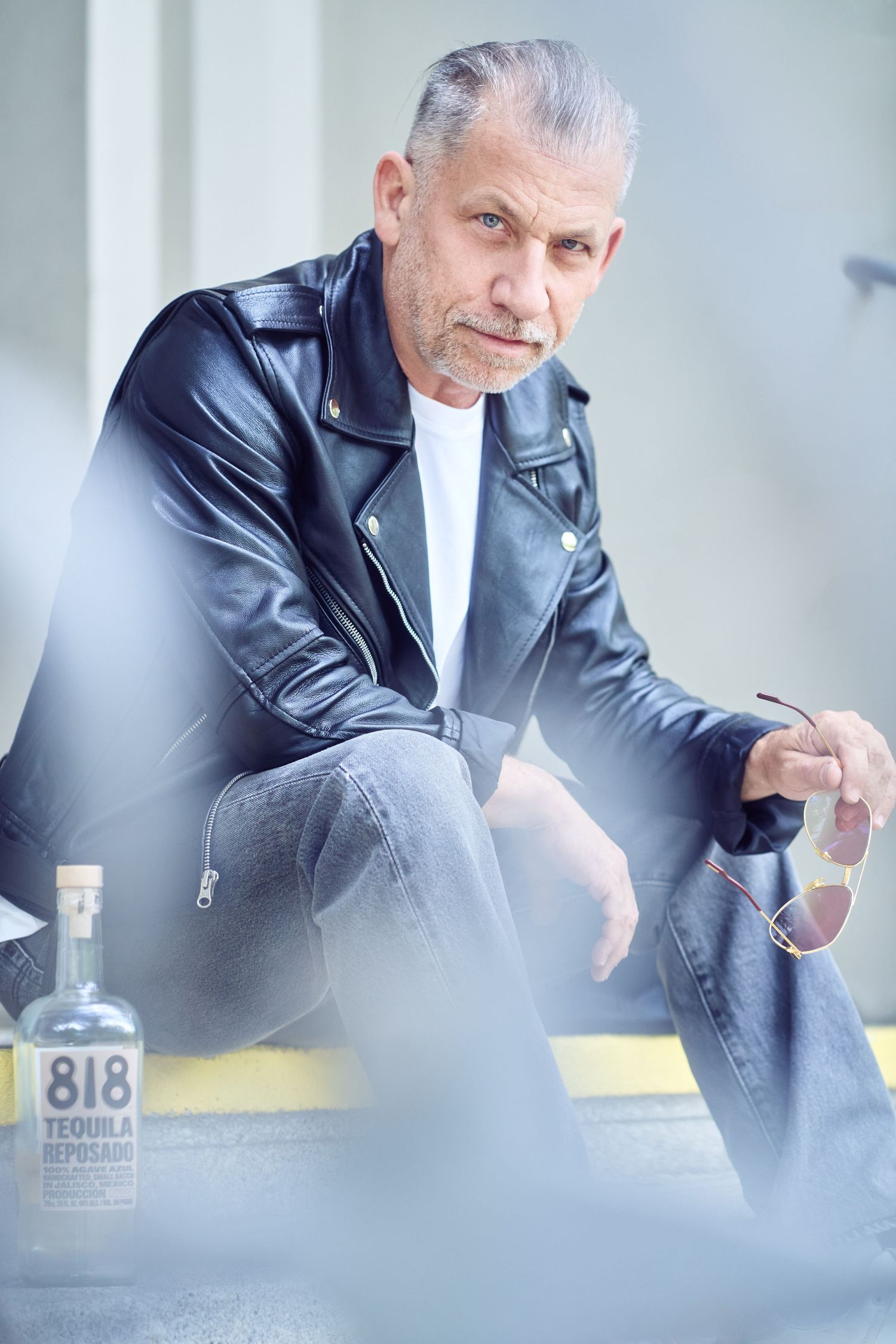 Mann in Lederjacke mit 818 Tequila Reposado Flasche, die Sonnenbrille auf einem stilvollen redaktionellen Foto hält.
