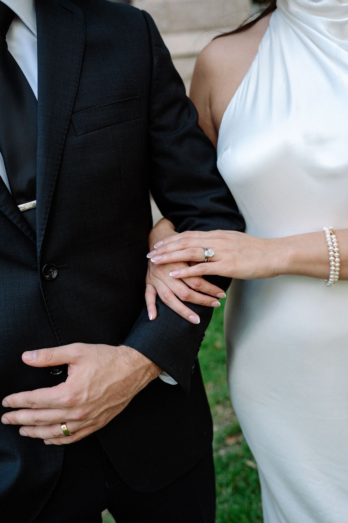 Close up of a a bride and groom's hands featuring a large oval engagement ring.