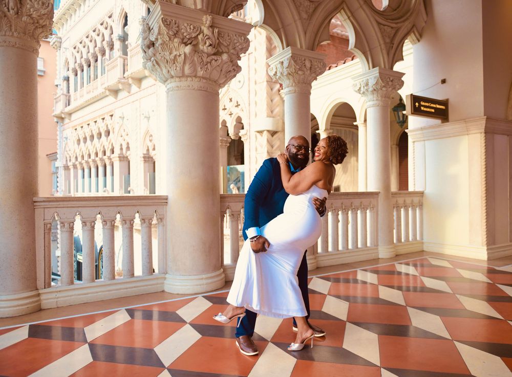 Couple embracing romantically under ornate arches at The Venetian Las Vegas, woman in white dress, man in navy suit.