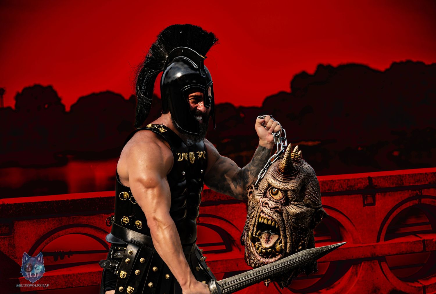 Muscular man in Spartan cosplay holds severed monster head prop against dramatic red background. Chi.Shooters meet tonybrettman