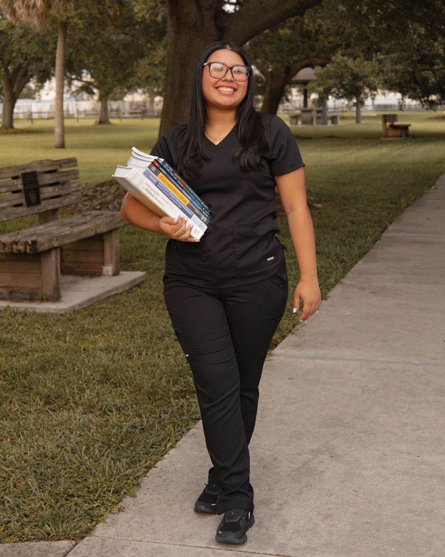 Smiling woman in black scrubs walking outdoors while carrying radiology textbooks.