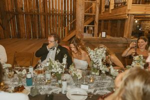 Bride and groom laughing at head table during rustic barn wedding reception with floral centerpieces.