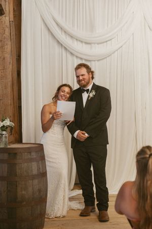 Bride and groom reading vows at rustic barn wedding with white draped backdrop.
