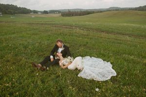 Bride and groom laying in lush green field during romantic outdoor wedding photo session.