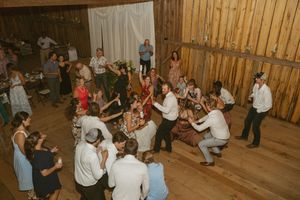 Wedding guests dancing joyfully inside rustic barn reception venue with warm lighting.