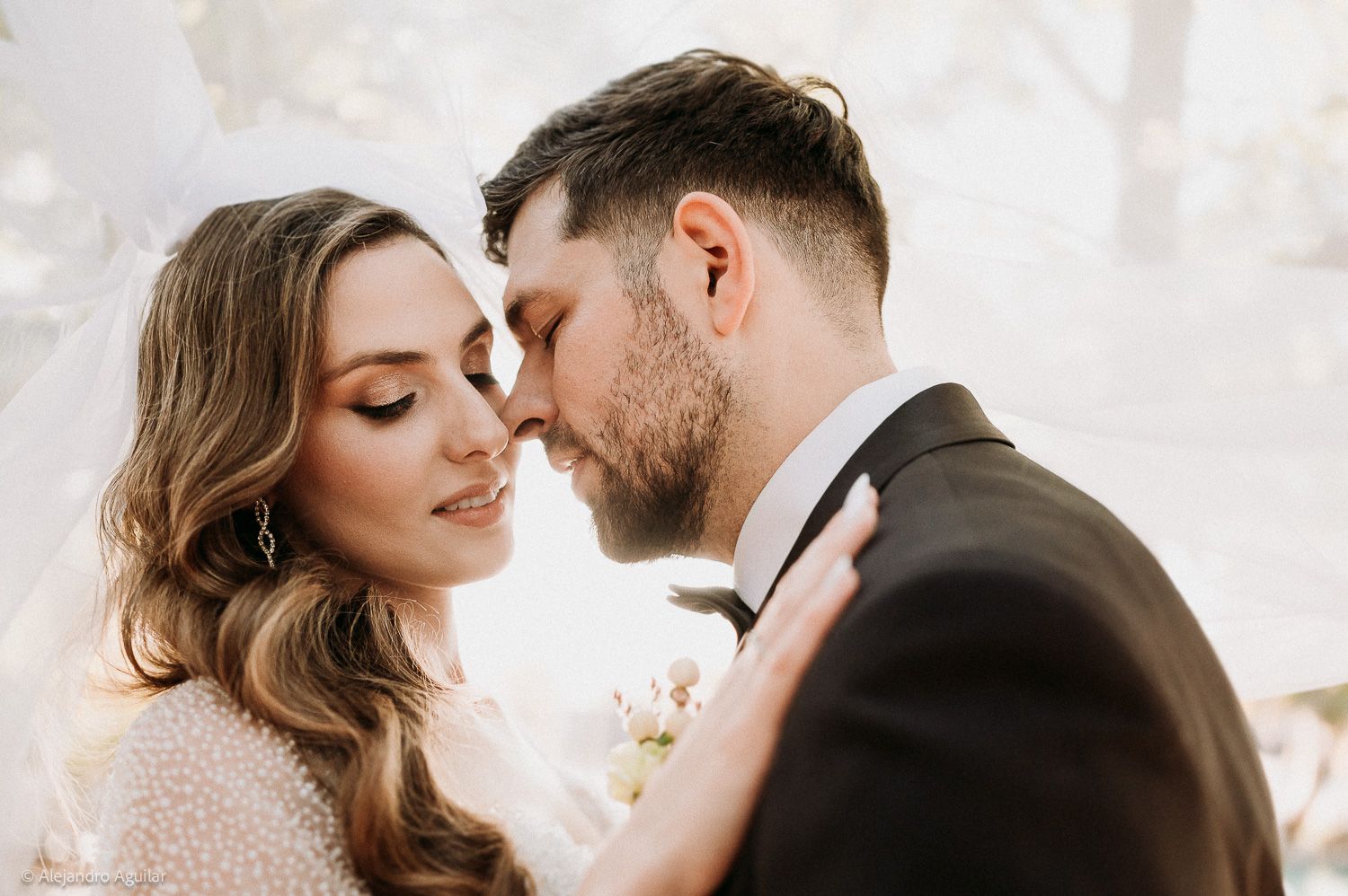 Romantic wedding couple sharing an intimate moment, bride in white gown with veil, groom in black suit with boutonniere.