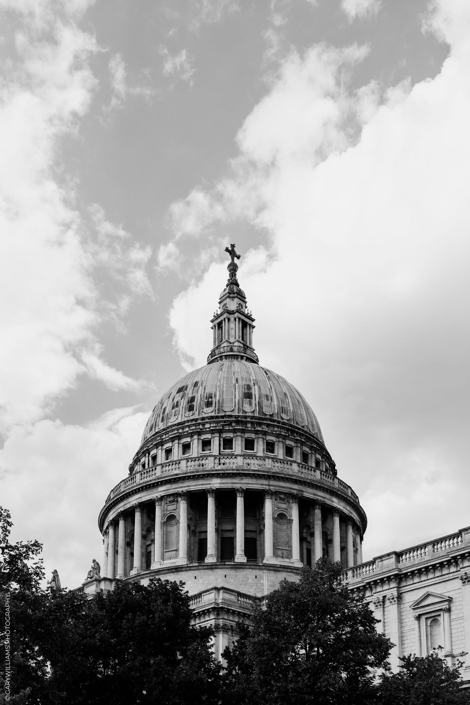 Black and white photo of St. Paul's Cathedral dome with cross against cloudy sky in London.